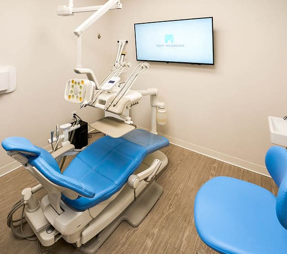 Spacious treatment room with a blue dental chair and patient TV at Troy Meadows Dental