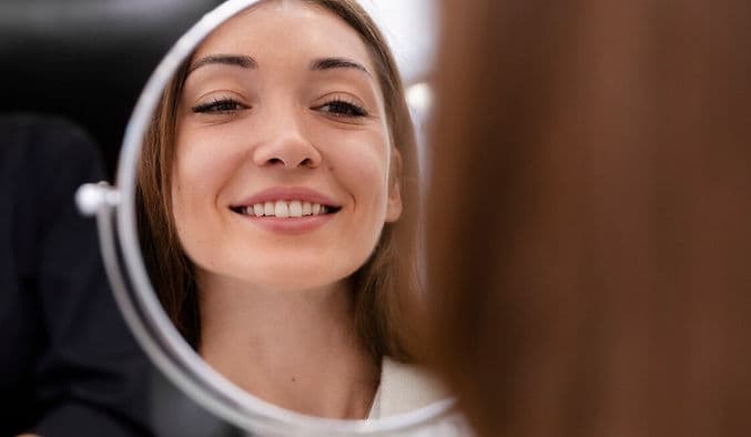Woman smiling at her reflection in a mirror after dental treatment